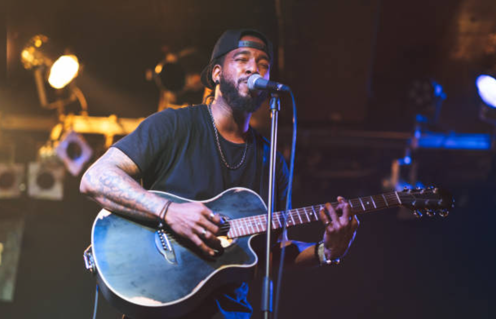 A musician playing acoustic guitar and singing into a microphone on a dimly lit stage